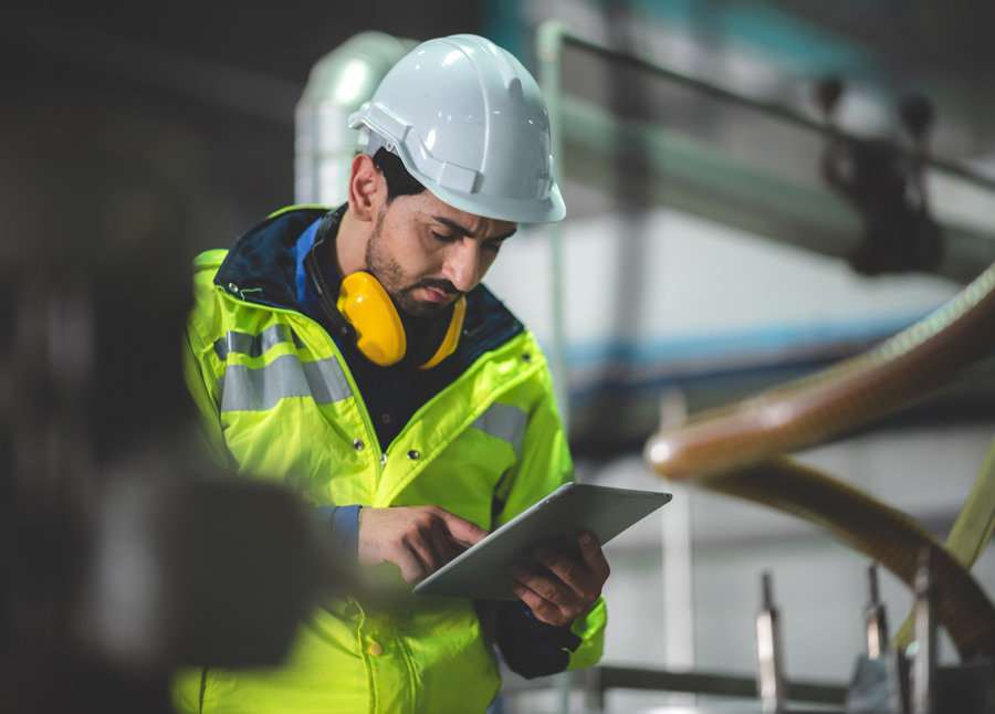 man in hardhat looking at a tablet device in industrial surrounding